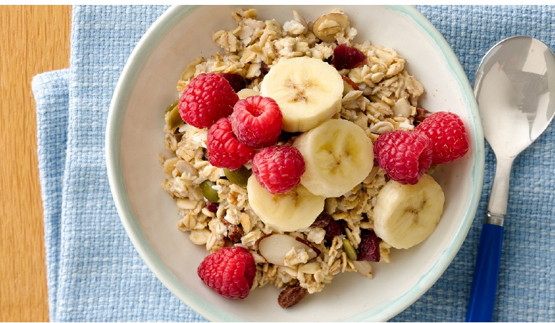 A bowl with Toasted Oats Muesli sprinkled on top of yogurt with sliced fruit and voila added