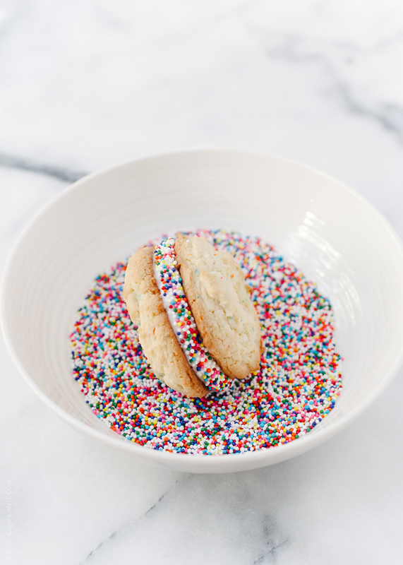 Dipping a birthday cake sandwich cookie into a bowl of colorful sprinkles.