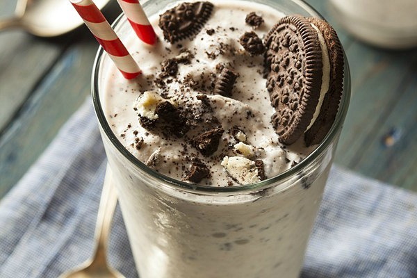 A close up of a Cookies and Cream Milkshake with Oreos sitting on top of it.